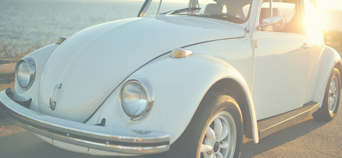 Image of VW Beetle driving along the coast with the sun shining in the background.