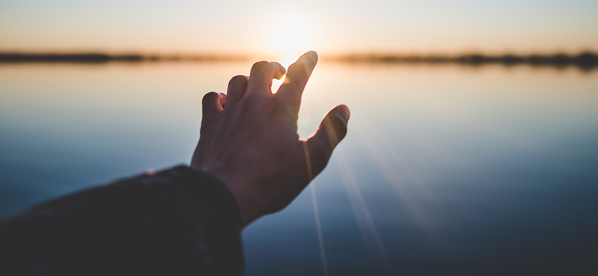 Person reaching for the horizon and touching the sun.